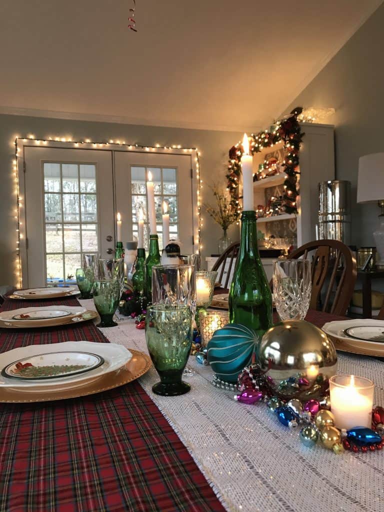 a Christmas table setting ready for Christmas dinner with a plaid table cloth, sparkling ornaments and lights and the glow of candles