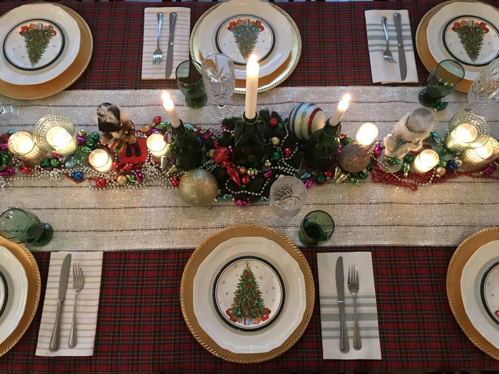 A Christmas table setting with a shimmering centerpiece studded with glowing candles, shimmering beads and ornaments