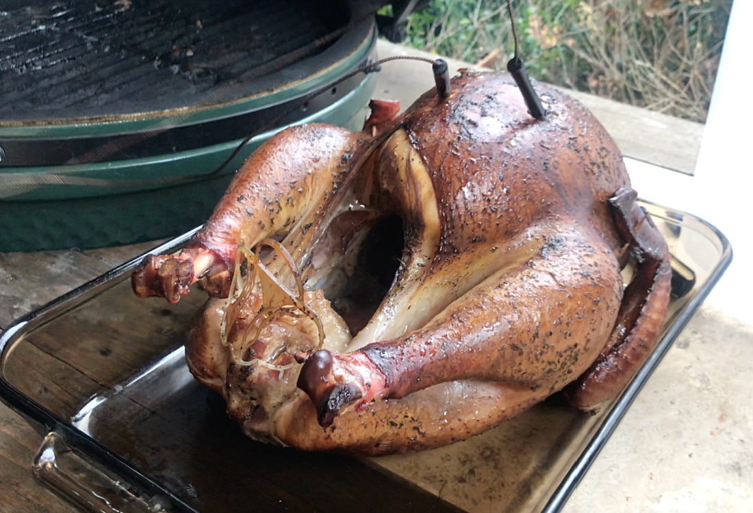 golden brown smoked turkey resting in casserole dish next to big green egg smoker - How to Brine a Turkey - Life Full and Frugal