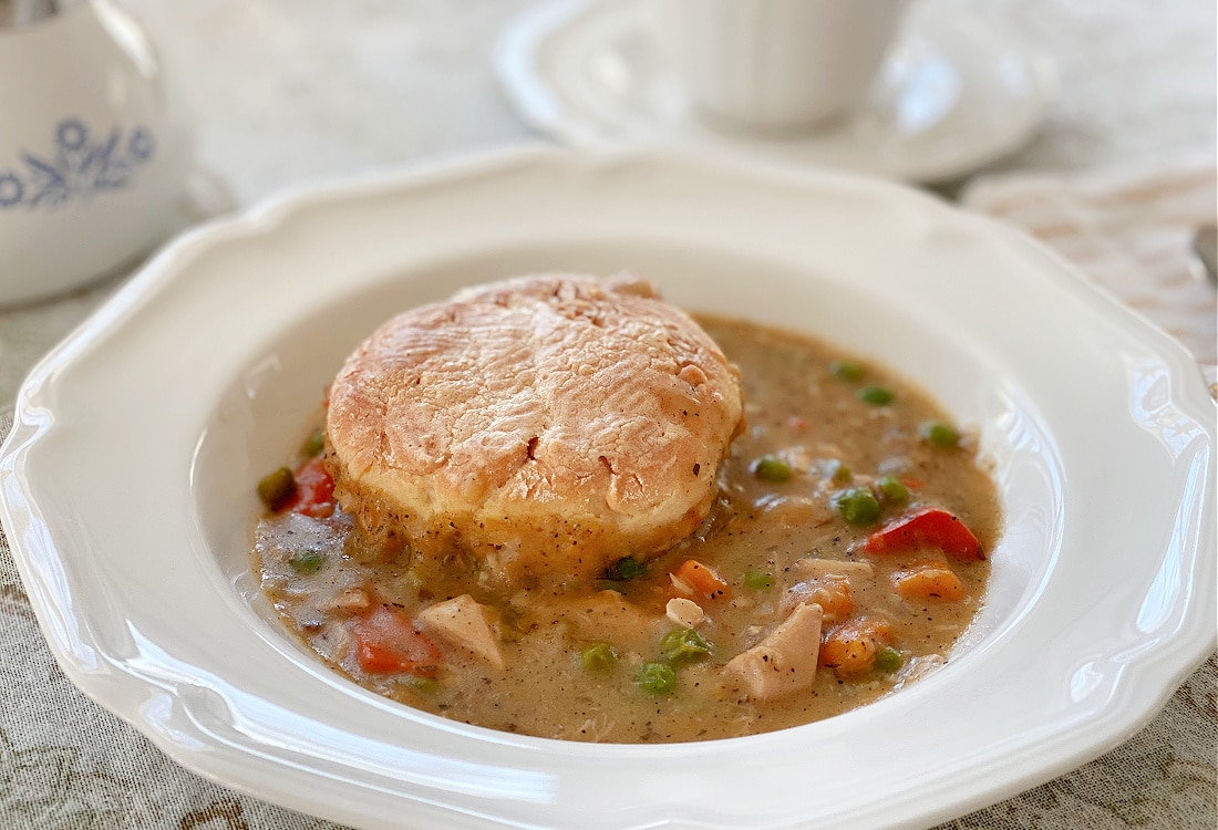 chicken biscuit pot pie served in a white, scalloped edged bowl - Dutch Oven Chicken Biscuit Pot Pie - Life Full and Frugal