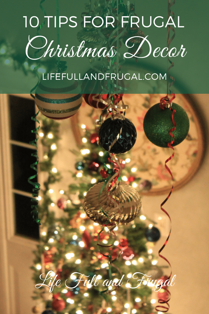 ceiling fan decorated with Christmas ornaments and curly ribbon with a Christmas tree lit up with lights in the background - 10 Tips for Frugal Christmas Decor - Life Full and Frugal
