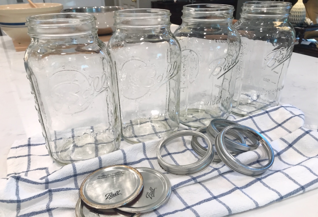 Simple Lacto-Fermented Sauerkraut - Life Full and Frugal - half gallon mason jars on a quartz countertop sitting on a blue and white dish towel with lids and rings at their bases
