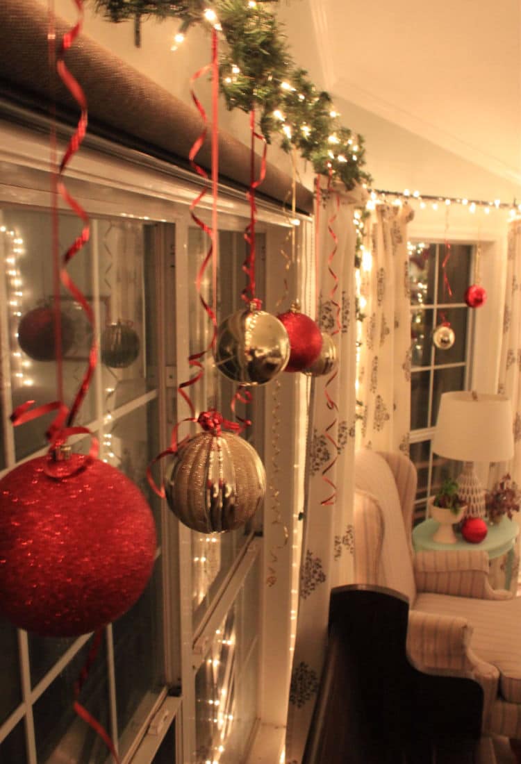 side view of a window framed in Christmas lights and garland with large Christmas bulbs hanging from ribbons draped across the top - 10 Tips for Frugal Christmas Decor - Life Full and Frugal