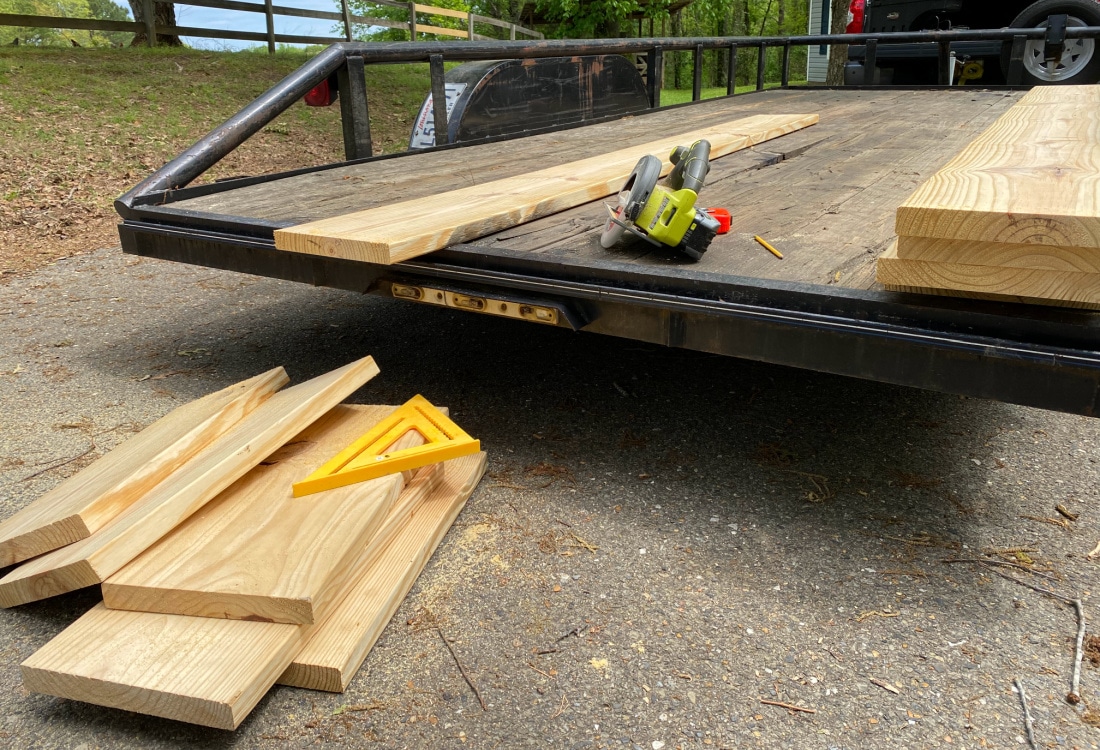 2x12 pine boards cut with a Ryobi battery powered circular saw and a speed square, cut boards piled on the ground in front of a flat bed trailer used as a work surface - DIY Raised Bed Garden Boxes - Life Full and Frugal