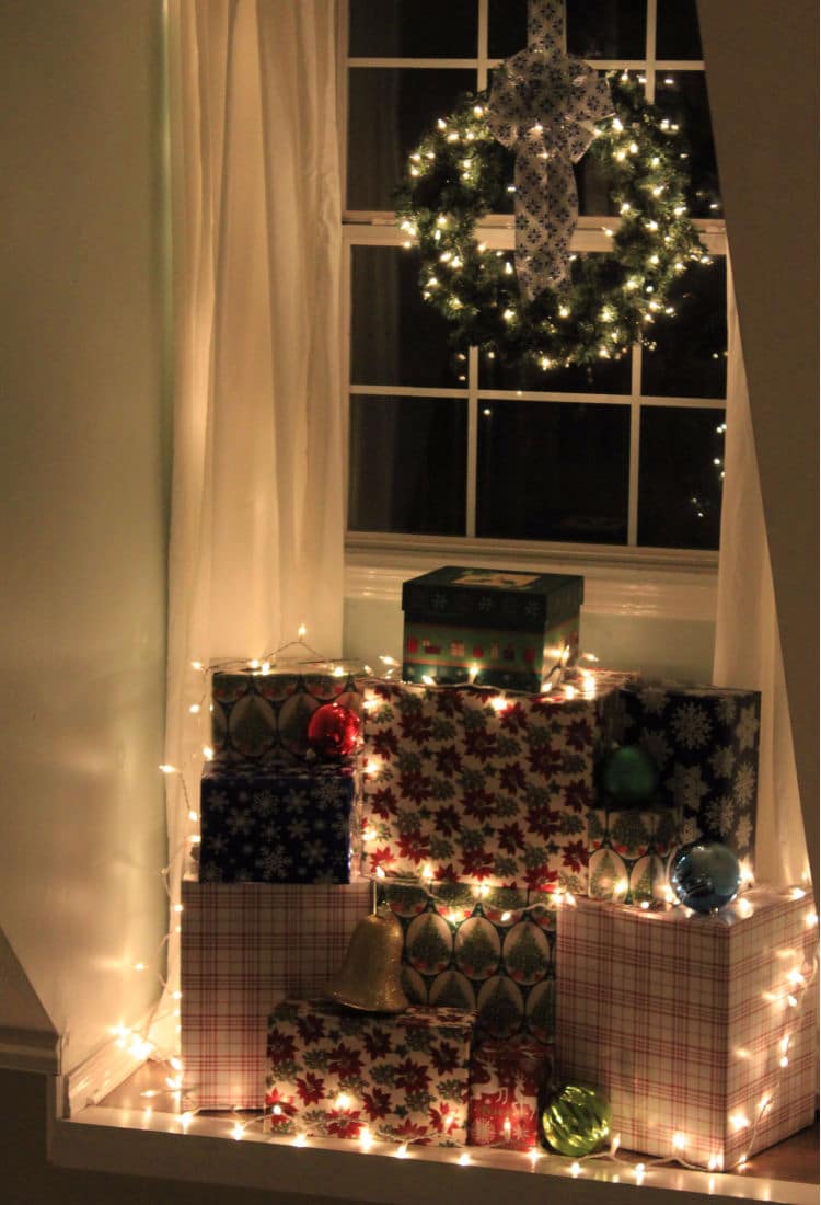window filled with wrapped Christmas boxes covered in Christmas lights and a wreath hanging in the window - 10 Tips for Frugal Christmas Decor - Life Full and Frugal