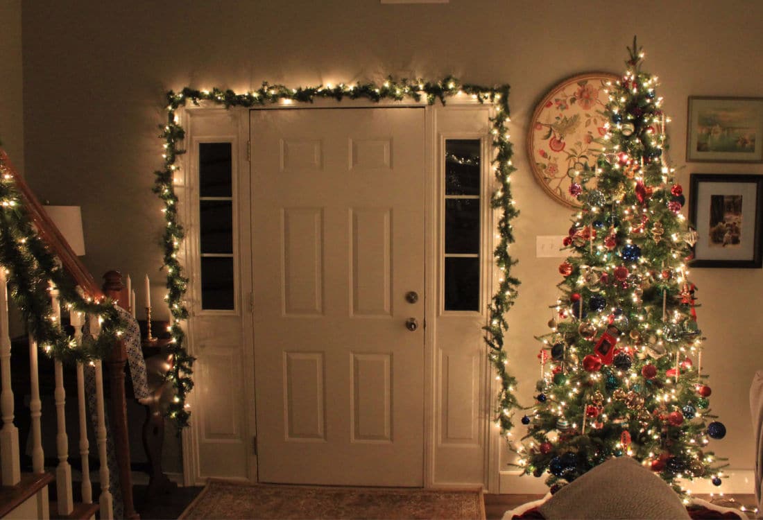 entry door framed in Christmas lights and garland with a  beautifully decorated Christmas tree next to it - 10 Tips for Frugal Christmas Decor - Life Full and Frugal