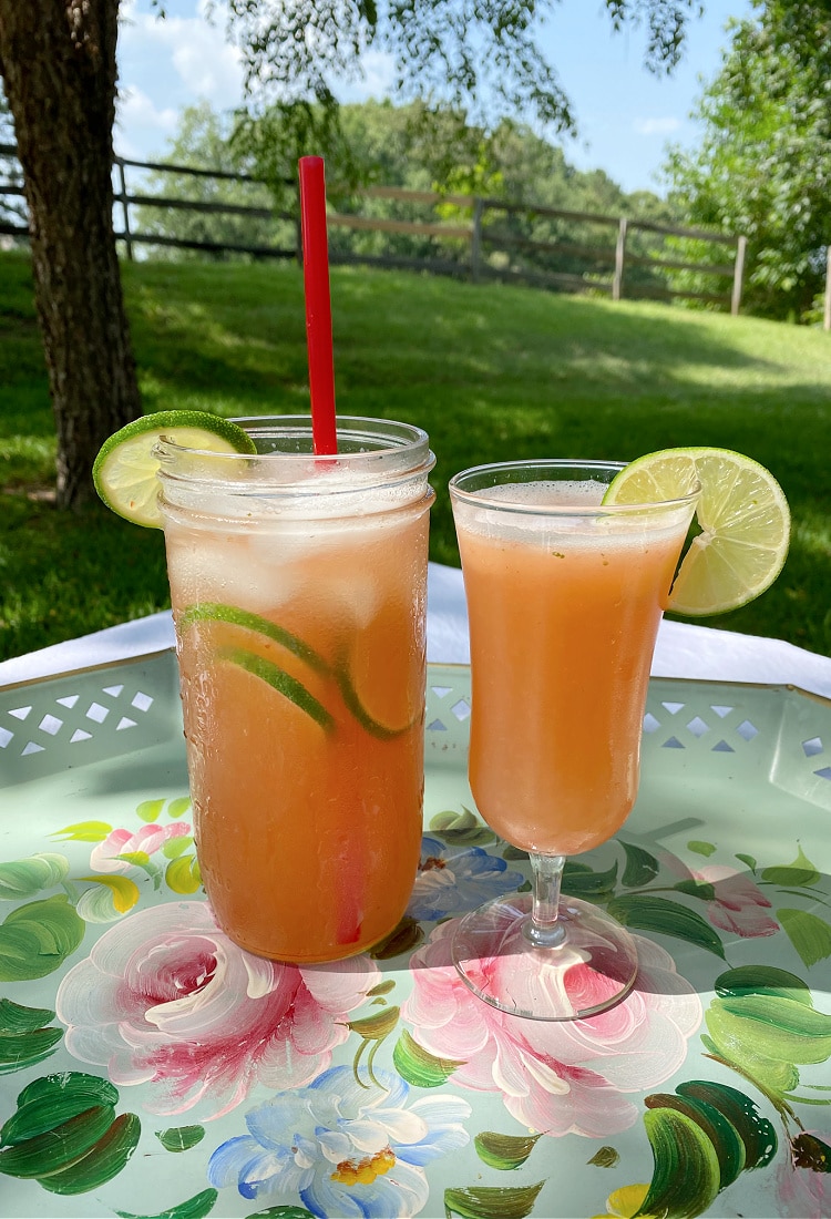 two strawberry limeade drinks garnished with limes one with a red straw sitting on a floral painted tray outside on a picnic table - Life Full and Frugal