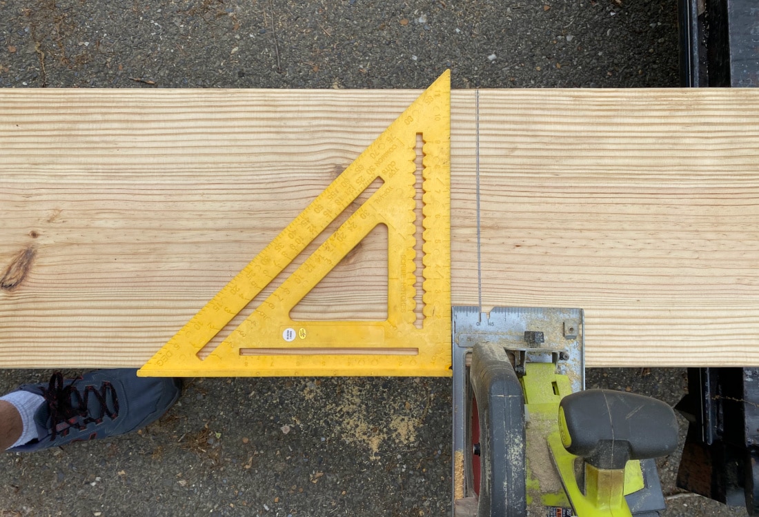 2x12 pine board with a speed square used as a guide for a Ryobi battery powered circular saw to make a straight cut - DIY Raised Bed Garden Boxes - Life Full and Frugal