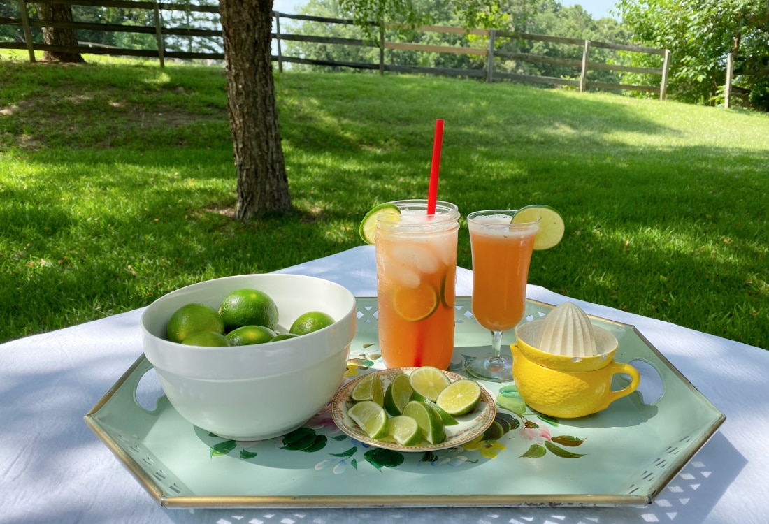 tray with a bowl of limes, a plate with sliced lime wedges next to a lemon shaped juicer with two strawberry limeade drinks in the middle - Life Full and Frugal