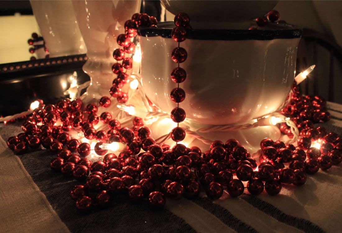 string of beaded garland draped over a planter pot lit up with Christmas lights - 10 Tips for Frugal Christmas Decor - Life Full and Frugal