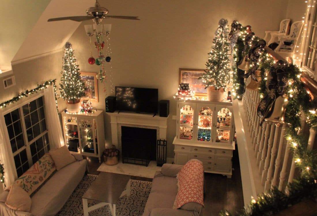 dimly lit living room decorated for Christmas with lights and ribbon and swags of garland over a stair bannister - Life Full and Frugal